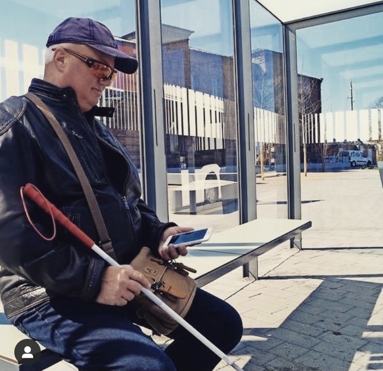 Der Sehbehinderte Olaf Hellwig sitzt mit dem Smartphone in der Hand in einer Bushaltestelle in Wittstock